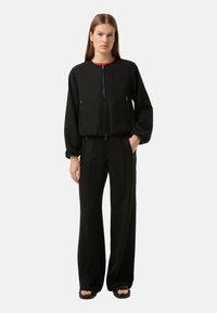 Czarna krótka kurtka bomberka z zamkiem, bocznymi kieszeniami i ściągaczami przy mankietach, zestawiona z wysokim stanem szerokich czarnych spodni.