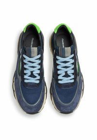 Pár tmavě modrých tenisek se světle modrými šněrováním, zelenými patními nášivkami, černými a béžovými podrážkami a proužkovanými štítky na jazyku, z pohledu shora.