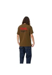 Camiseta de algodón marrón con texto gráfico rojo en la parte posterior. Mangas cortas y ajuste relajado, combinada con jeans azul oscuro.