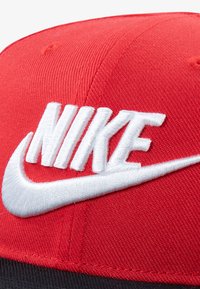 R ød kasket lavet af tekstureret stof med en fremtrædende hvid broderet "NIKE"-logo og en buet skygge.