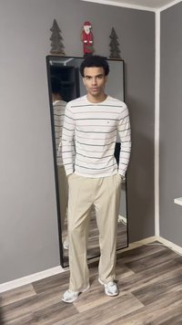 Λευκό πουκάμισο με μακριά μανίκια και οριζόντιες μαύρες και ροζ ρίγες, συνδυασμένο με μπεζ παντελόνια και λευκά αθλητικά παπούτσια. Καθρέφτης στο φόντο.