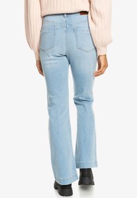 Jeans a zampa d'elefante blu chiaro con vita media, design a cinque tasche e una trama di denim liscia. Abbinati a un maglione rosa a coste e stivali neri.