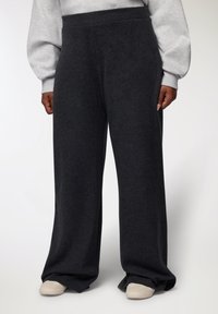 Pantaloni larghi grigio scuro realizzati in un tessuto morbido e texture, con vita alta e senza chiusure visibili, abbinati a scarpe chiare.