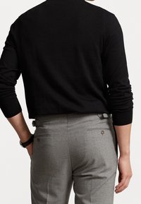 Suéter negro de manga larga, tejido texturizado, combinado con pantalones grises ajustados con bolsillos traseros y acentos sutiles.