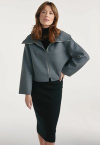 Szary skrócony żakiet z dużym kołnierzem i pełnym zamkiem z przodu, w połączeniu z czarną prążkowaną spódnicą ołówkową, na neutralnym tle.