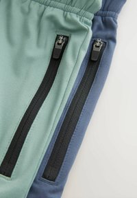 Atletické kalhoty v teal a modrých segmentech se dvěma černými kapsami na zip na stranách, elastickým pasem a hladkým směsovým bavlněným materiálem.