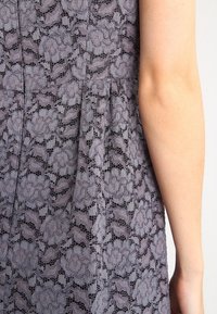 Robe en dentelle grise avec des motifs floraux, une surface texturée et un design plissé ; épaule visible sur le côté droit.