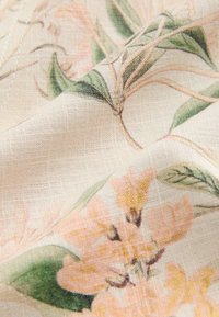 Tissu floral présentant des fleurs douces roses et jaunes sur un fond beige, avec une texture légèrement tissée.
