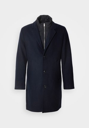 Merinovillasekoitteen tummansininen takki, jossa on leikattu kaulus, viisi etupainiketta, sivutaskut ja musta eristetty vuori. Puolipitkä malli.