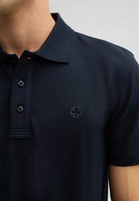 Marineblaue Polohemd aus strukturiertem Stoff, mit einer Knopfleiste mit drei Knöpfen und einem dezenten, eingeprägten Logo auf der linken Brust.
