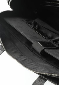 Interior de un bolso de cuero negro con compartimento con cremallera, forro de tela suave, bolsillos elastizados y un diseño elegante y minimalista.