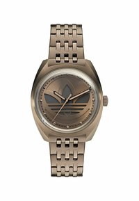 Pronksist kell, millel on matt pruun nägu, embosseeritud logo, kitsenevad tunni- ja minutinäpud ning kootud randmehääl.