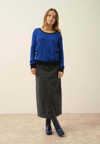 Modrý svetr s černým výstřihem, v kombinaci s dlouhou černou džínovou sukní a modrými kotníkovými botami, na neutrálním pozadí.