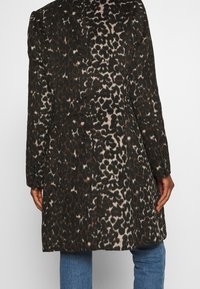 Leopardmönstrad kappa med mörkbrunt och beige mönster, klassisk design, enkelknäppt stängning och detaljerade knappaccentuer.