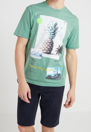Zielona bawełniana koszulka z graficznymi nadrukami przedstawiającymi ananasa i palmy, wzbogacona okrągłym akcentem oraz detalami tekstowymi.