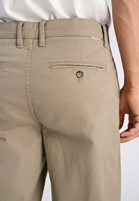 Beige broek van een katoenmix, met twee achterzakken met knoopsluitingen, riemlussen en een zachte, gestructureerde afwerking.