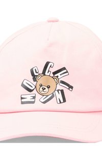 Gorra rosa claro con la cara de un osito de peluche en el centro, rodeada de letras negras y blancas dispersas que forman la palabra "MOSCHINO."