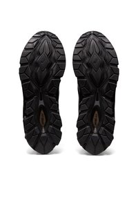 Černé podrážky atletických bot s texturovaným, robustním vzorem. Mají hluboké drážky pro lepší trakci, zesílené části a hladkou oblast mezipodešve.