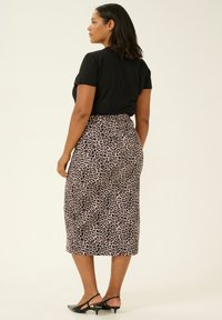Jupe midi en imprimé léopard, fabriquée en tissu lisse, avec une taille haute et une coupe slim, associée à un haut noir à manches courtes et des sandales à talons noires.
