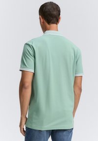 Hellgrünes Polohemd mit kurzen Ärmeln und einem kontrastierenden weißen Kragen sowie Ärmelsaum, in lockerem Schnitt und mit glatter Textur.
