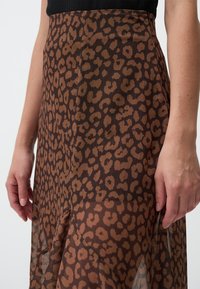 Jupe à imprimé léopard dans des tons marron et beige, fabriquée en tissu transparent. Présente un design fluide avec une texture douce et des fentes sur les côtés.