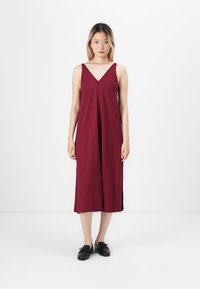 Burgunderfarget, ermeløs kjole med V-hals og flytende design, i midi-lengde. Laget av myk stoff, minimalistisk stil.