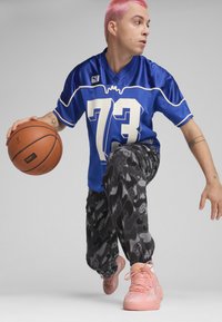 Jersey de malla azul con acentos blancos y el número 73, pantalones deportivos negros con un diseño estampado que presenta motivos deportivos, y zapatillas de deporte de color rosa claro.