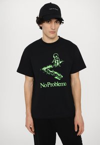 Sort bomuld t-shirt med et grønt grafisk design af en alien og teksten "No Problemo" nedenunder. T-shirten har korte ærmer og rund halsudskæring.