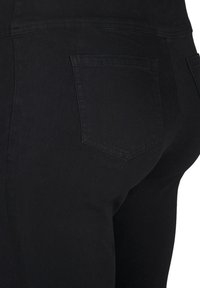 Jeans de mezclilla negra con un corte ajustado, que presentan un bolsillo trasero estándar y una textura suave, mostrados desde un ángulo lateral.