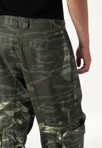 Cargo-byxor i mörkgrön kamouflage, med sidofickor, ett robust midjeband och synliga sömmar längs sömmarna.