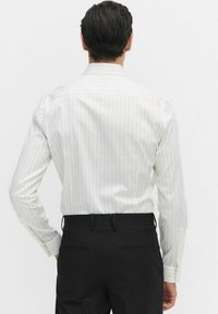 Witte langemouwen shirt met dunne verticale zwarte strepen, voorzien van een klassieke kraag en knoopmanchetten, gecombineerd met zwarte pantalon.