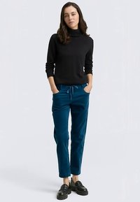 Fekete bordázott garbó pulóver, párosítva tengerzöld bársony nadrággal, melyen húzózsinór van a derékrésznél, és fekete fűzős cipő, a hétköznapi megjelenésért.