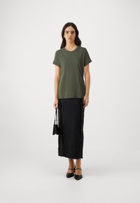 T-shirt en coton vert olive à manches courtes associé à une jupe en denim noire avec des bords effilochés, portée avec un petit sac à main noir.