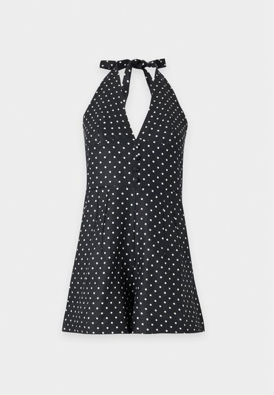 Μαύρο ολόσωμο μαγιό τύπου halter neck με λευκές βούλες, κουμπιά μπροστά και ελαφρώς φαρδιά σορτς σε απλό ανοιχτό φόντο.