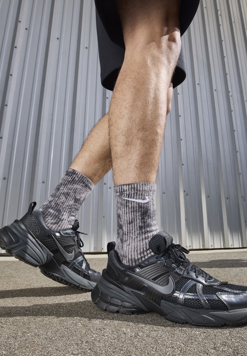 Black athletic sneakers with textured mesh, contrasting shiny accents, and thick soles, paired with gray striped crew socks featuring a logo.