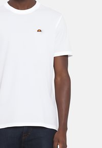 T-shirt bianca a maniche corte in cotone, con un piccolo logo ricamato arancione e giallo sul lato sinistro del petto. Collo rotondo, vestibilità slim.