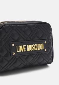Černá prošívaná kožená taška s pozlacenou nálepkou "LOVE MOSCHINO" na černém pozadí a zlatými kovovými doplňky. Uzavírání na zip.