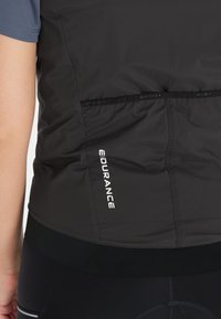 Sort letvægtsvest med en tekstureret overflade, der har hvid "ENDURANCE" branding. Kombineret med en sort strækbar talje for bedre pasform.