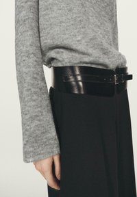 Czarny skórzany pasek o gładkim wykończeniu z detalem klamry, zestawiony z szarym dzianinowym swetrem o fakturowanym wzorze i długich rękawach.