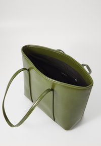 Sac fourre-tout en cuir vert avec deux poignées, de forme rectangulaire, texture lisse, et un intérieur noir avec une poche zippée.