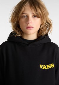 Felpa nera con cappuccio realizzata in tessuto morbido, con il logo giallo Vans sul lato sinistro del petto. Il design include un cappuccio a strati e una vestibilità classica.