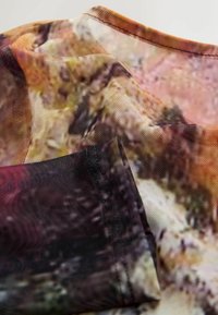 Przezroczysta tkanina z abstrakcyjnym wzorem w ciepłych, ziemistych odcieniach, o gładkiej fakturze i delikatnym przeszyciu na brzegach.