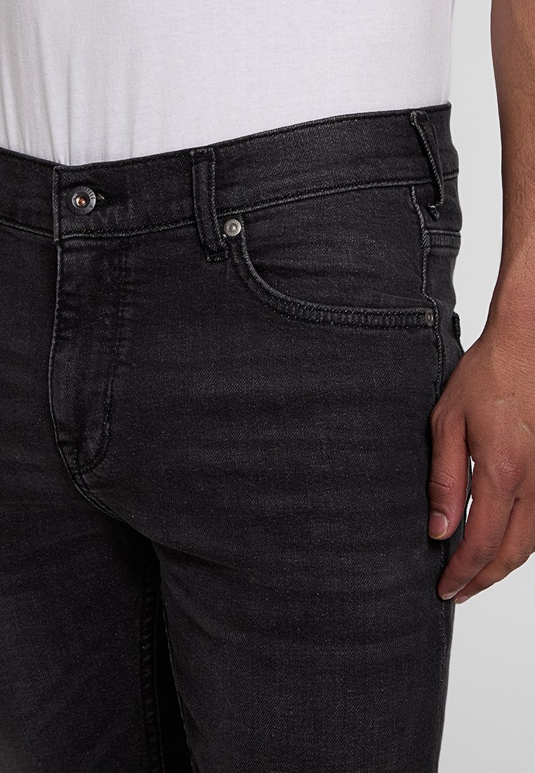 Czarne dżinsy z denimu z klasycznym pięciopocketowym fasonem, metalowym zapięciem na guzik i lekkim przetarciem na tkaninie dla nadania tekstury.