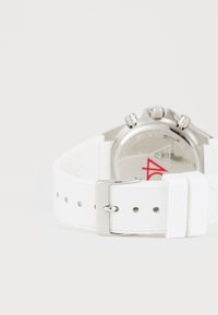 Witte horloge met een gestructureerde band, zilveren hardware en een decoratieve chronograaf wijzerplaat met rode accenten. De achterkant is glad en metallic.