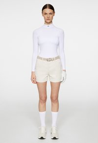 Biała bluzka z długim rękawem, beżowe szorty, jasny pasek z klamrą, białe rękawiczki, białe skarpetki i jasne trampki. Prosty, dopasowany krój.