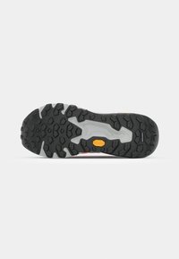 Semelle de chaussure de randonnée noire et grise avec des crampons profonds multidirectionnels et un petit logo Vibram jaune au centre.