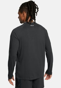Sort langærmet træningsshirt med rund hals og en glat tekstur. Har et lille "TRAIL"-logo i nakken på bagsiden.