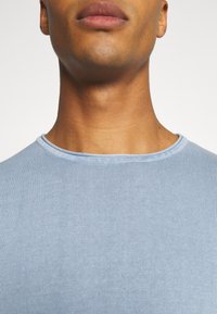 Hellblaues, geripptes Strick-T-Shirt mit Rundhalsausschnitt und slim fit, glatter Textur und minimalem Nähdetail am Kragen.