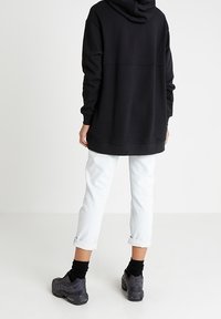 Svart huvtröja med långa ärmar, kombinerad med ljusblå jeans med uppvikta ärmar och mörka träningsskor. Enkel design, ledig passform.