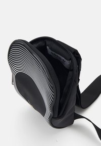 Černá textilní taška přes rameno se horizontálním bílým pruhem, zapínáním na zip a vnitřním oddělením, s visačkou Adidas.